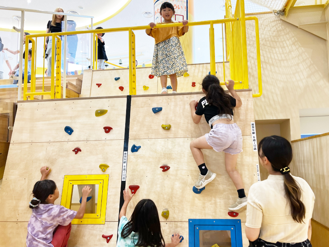 施設内のロッククライミングを登り遊ぶ子供たちの写真