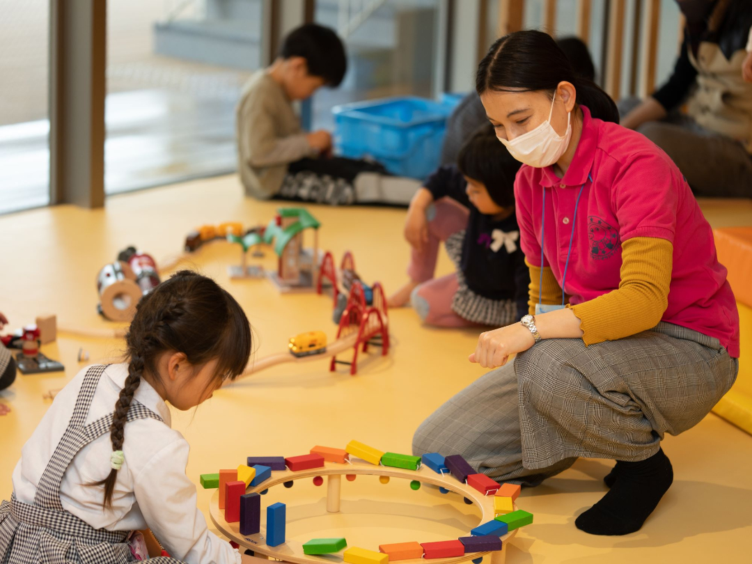 スタッフと子供がおもちゃで遊んでいる写真