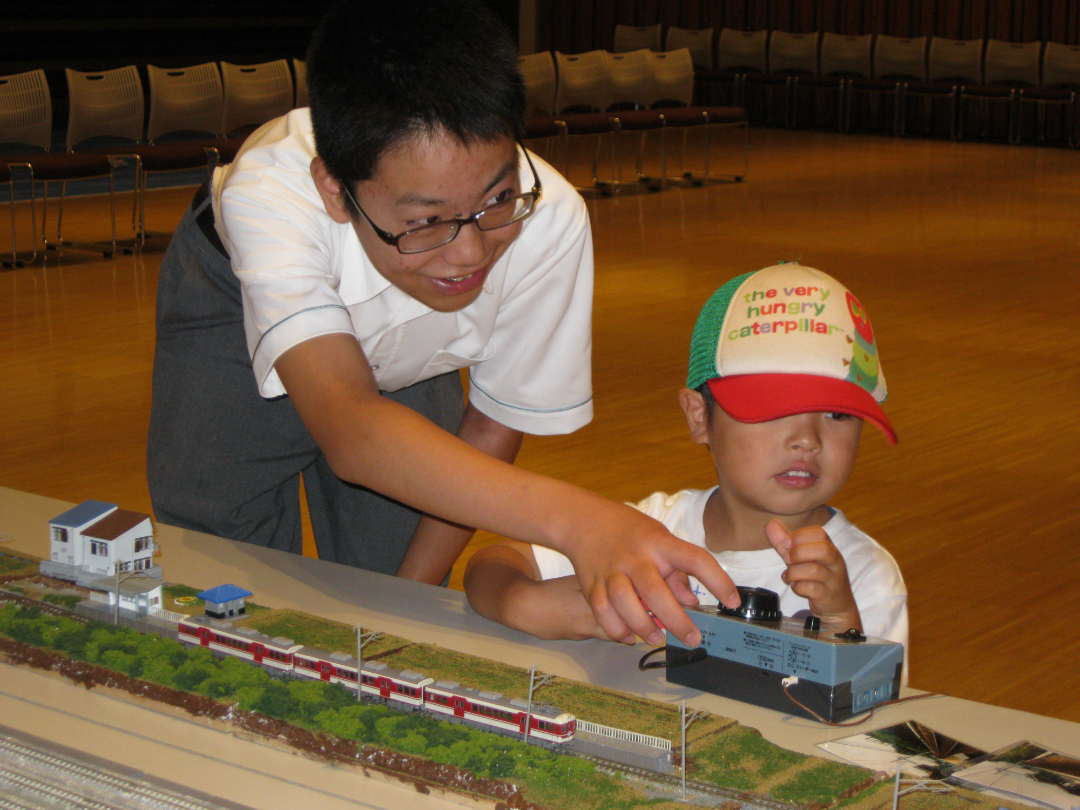 中高生と子供が電車のおもちゃで遊んでいる写真