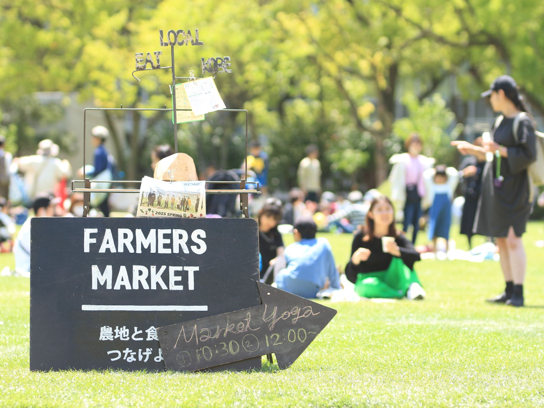 芝生の上にフリーマーケットの看板が置かれ、人が集まって楽しんでいる写真