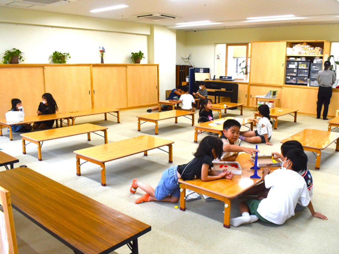テーブルが並べられている室内で、子供たちがそれぞれ遊んだり勉強をしている写真