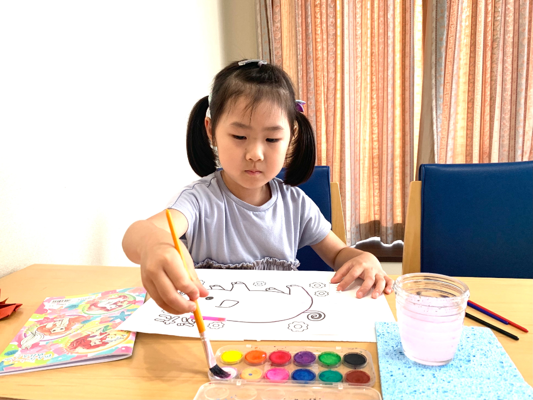 絵具と画用紙を広げ、懸命に塗り絵を楽しむ子供の写真