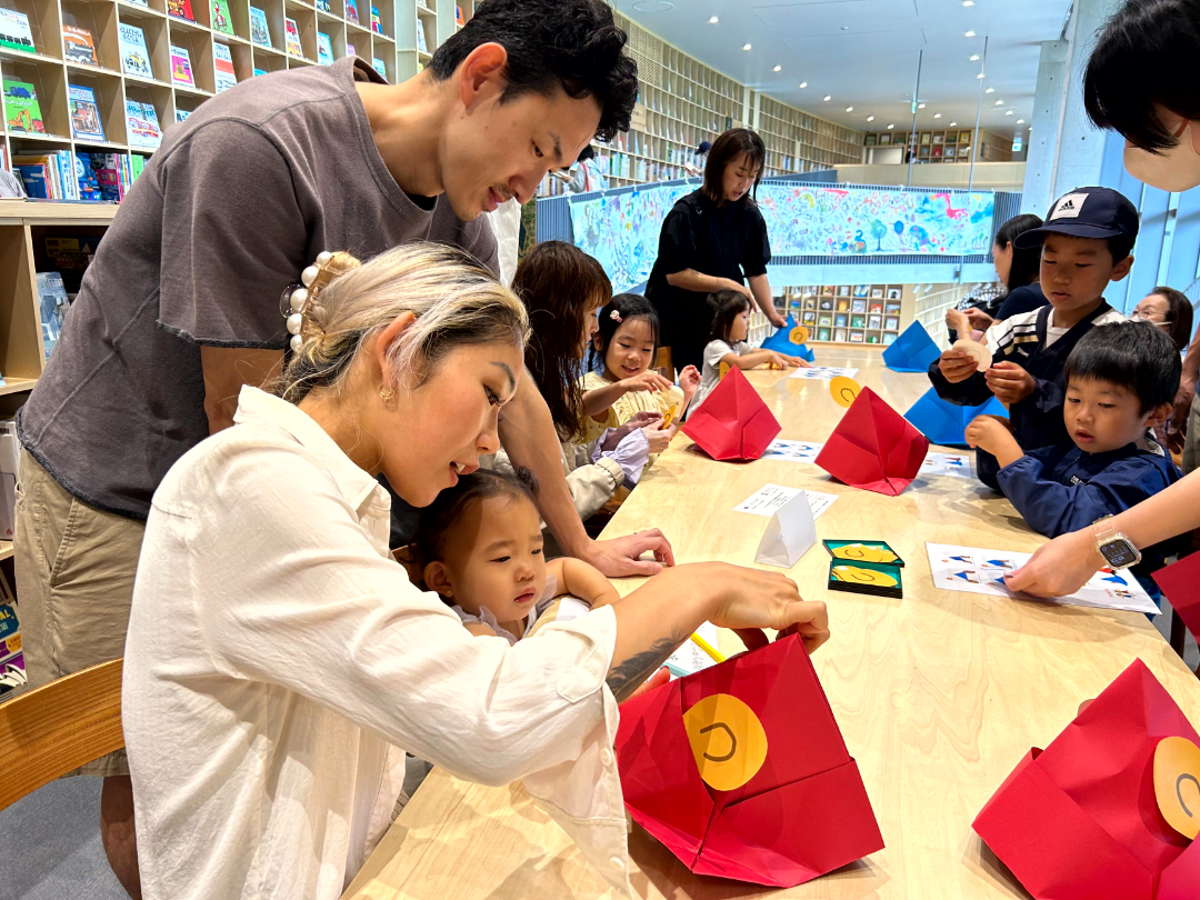赤色の帽子を紙で折り作成する親子の写真