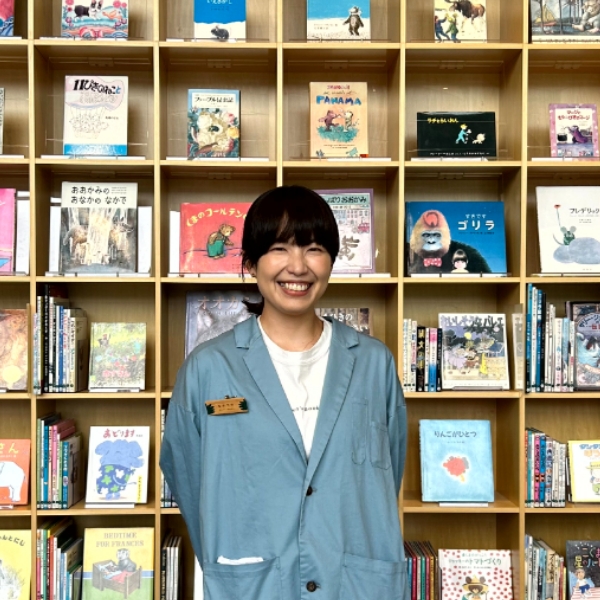 本棚をバックに笑顔で映る中塚さんの写真