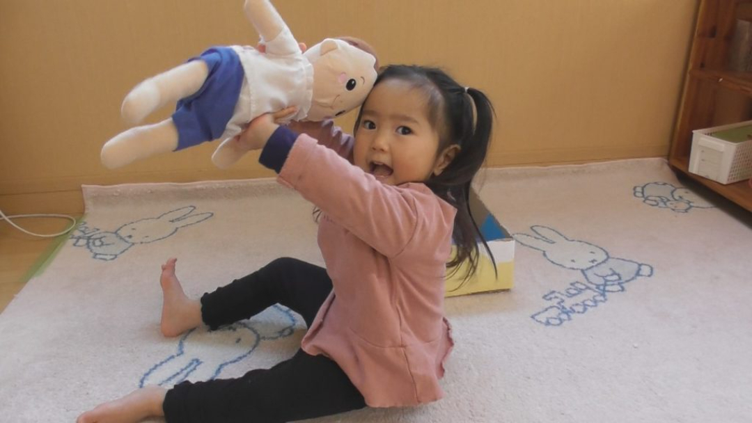 2歳前後の女の子が床に座って人形遊びをしている写真