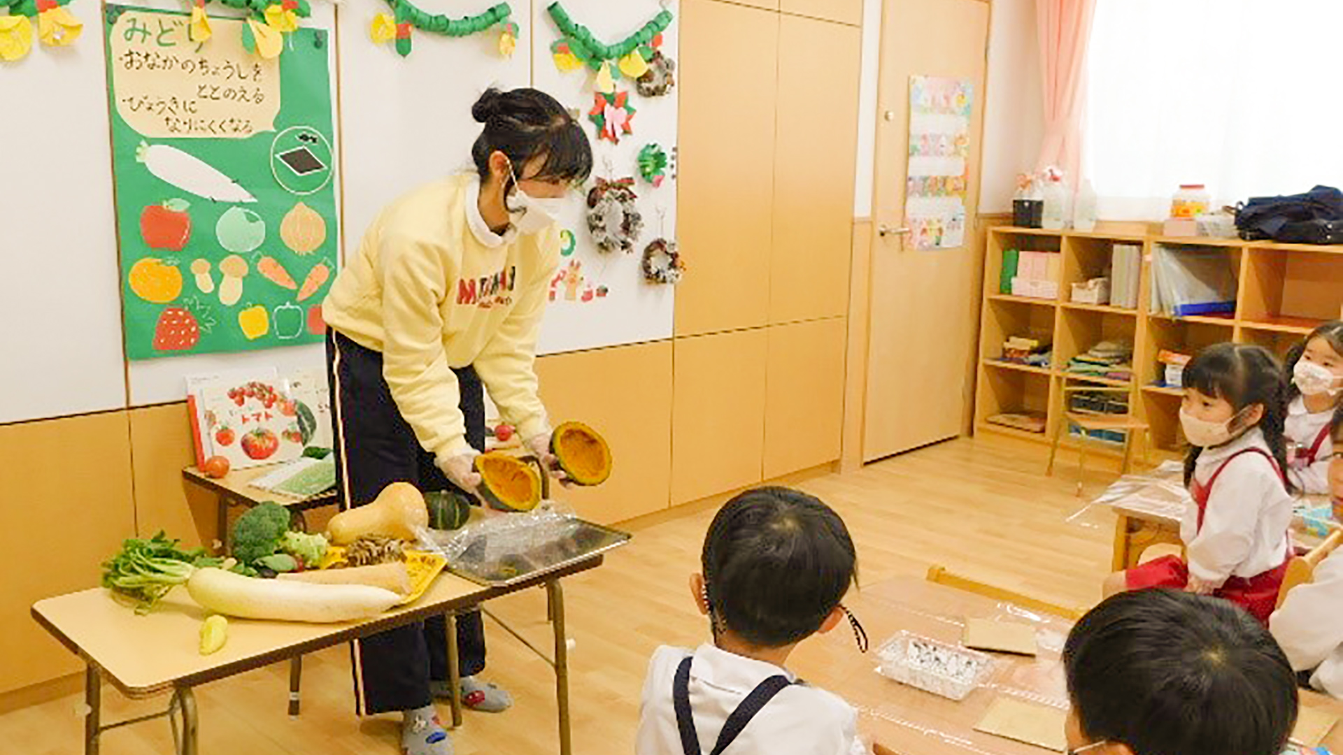 保育園の先生が子どもに野菜を見せている様子