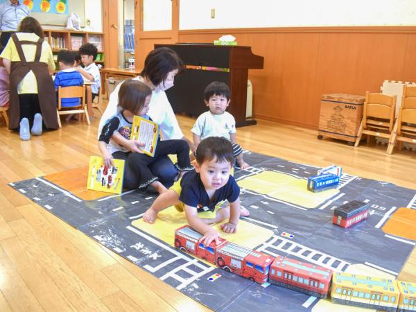 電車のおもちゃで遊んでいる子供と、子供を膝にのせて一緒に遊ぶ先生の写真